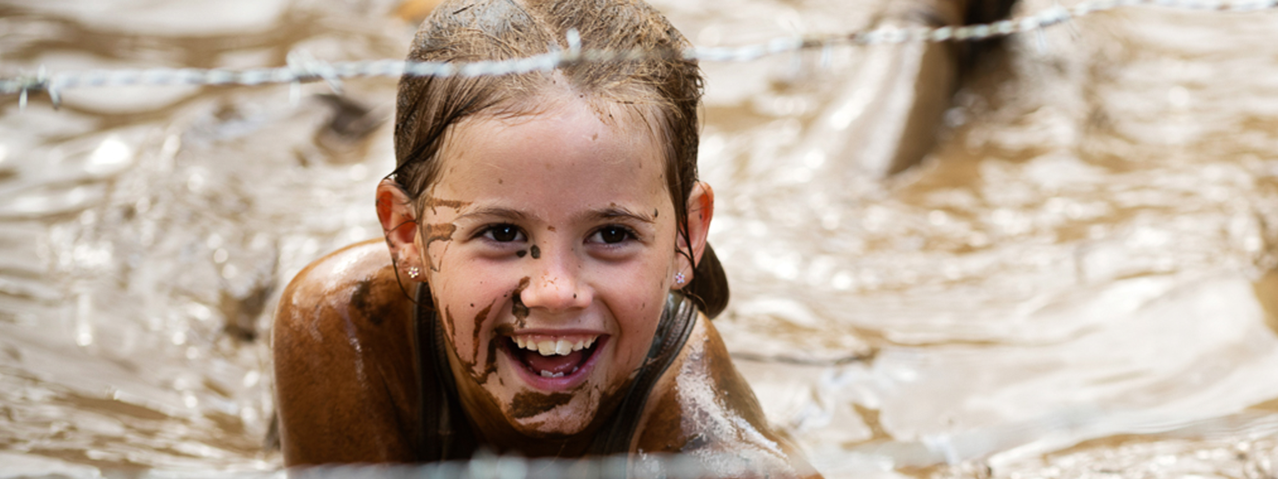 een meisje dat lachend door de modder kruipt tijdens de family editie van strong viking amsterdam