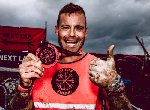 een ultra viking deelnemer die onder de modder zit en een medaille vasthoudt
