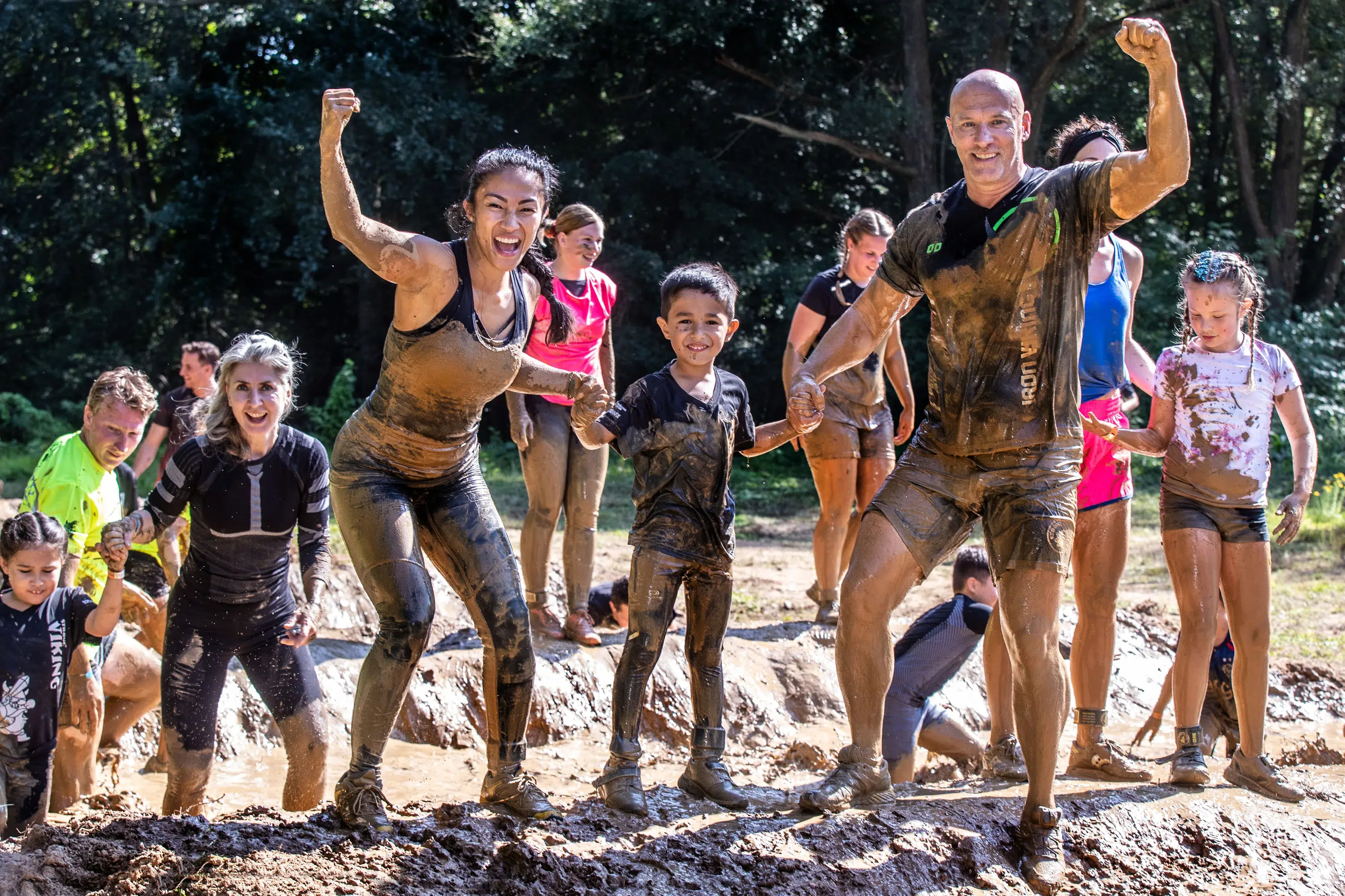 Kinderen en volwassenen die door de modder lopen en hun spierballen laten zien tijdens de Obstacle run Mud editie